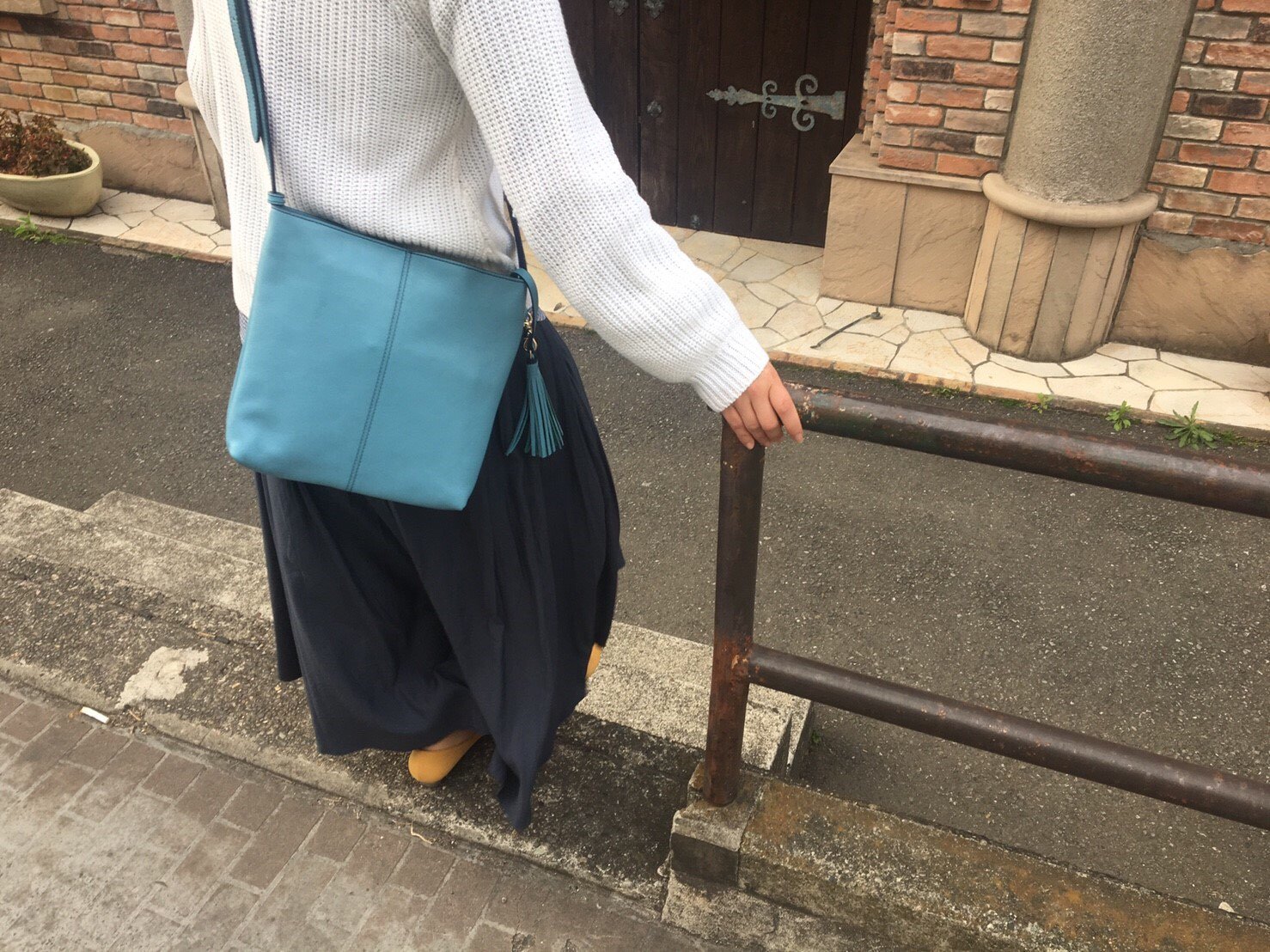 青いショルダーバッグを持って歩道で立っている女性