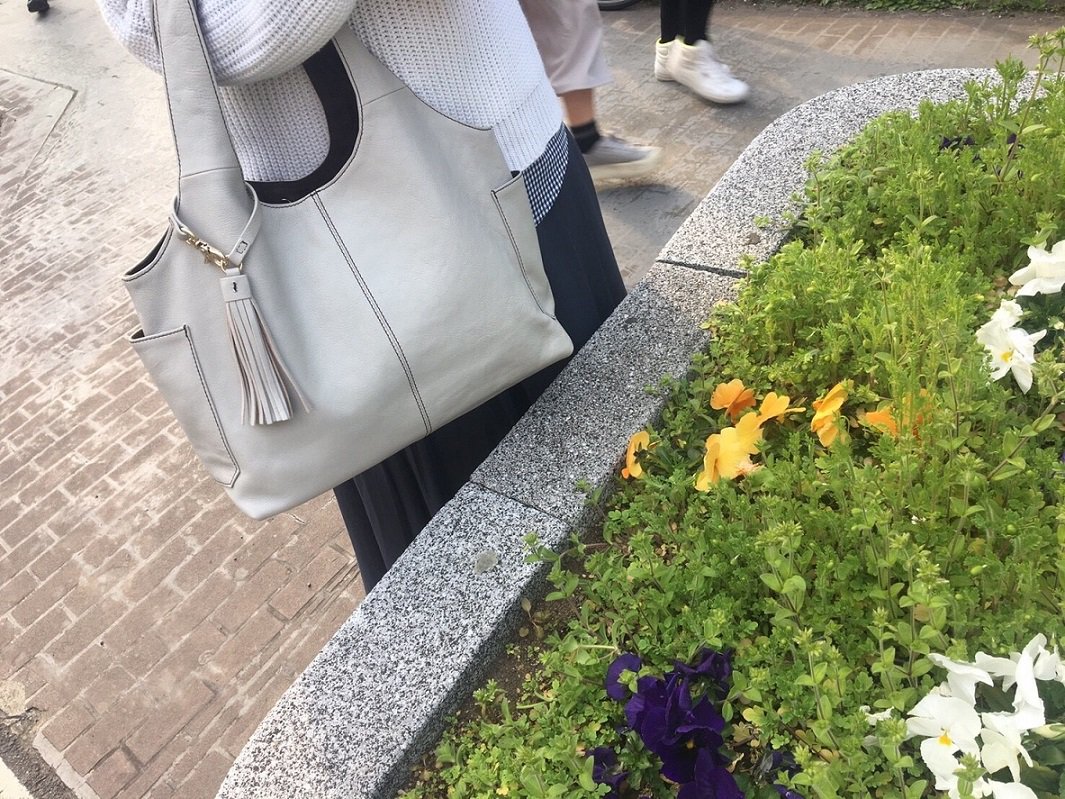 白いトートバッグを持って花壇の横で立っている女性